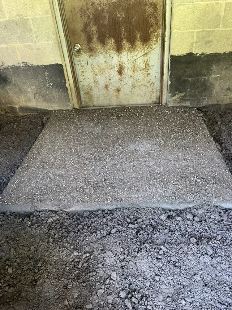 Raised concrete pad outside the basement door with surrounding gravel beside the block foundation
